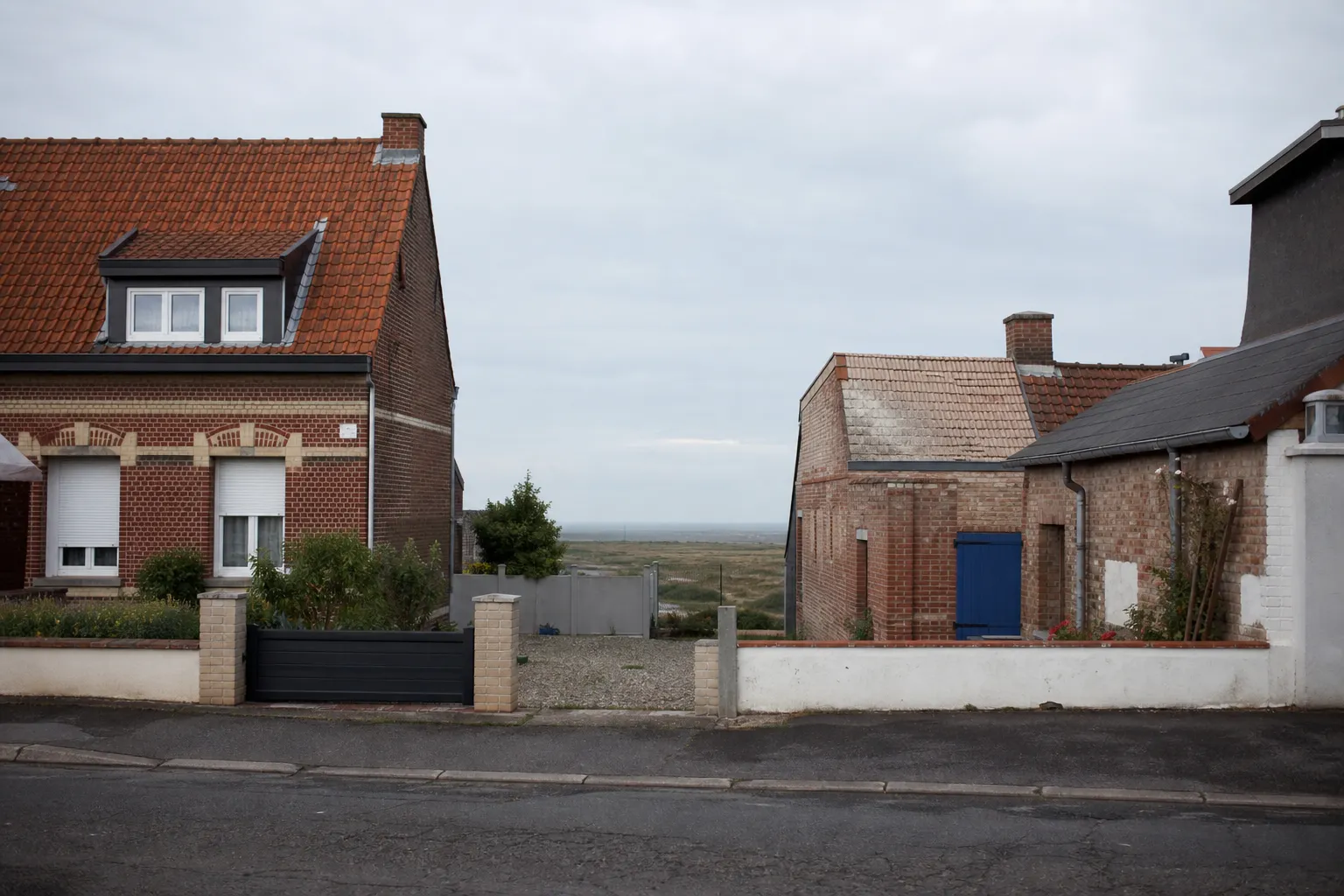 Rue résidentielle de Coulogne dans le Pas-de-Calais, maisons de brique aux toitures en tuile, ciel couvert du littoral, photographie documentaire sans personne