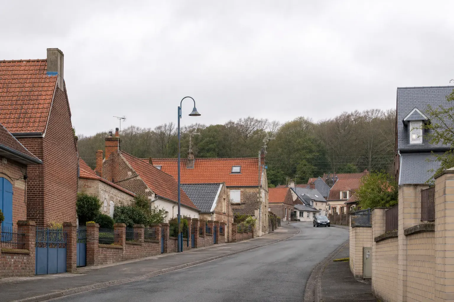 Rue résidentielle de Guînes dans le Pas-de-Calais, maisons de brique aux toitures en tuile, ciel couvert du littoral, photographie documentaire sans personne