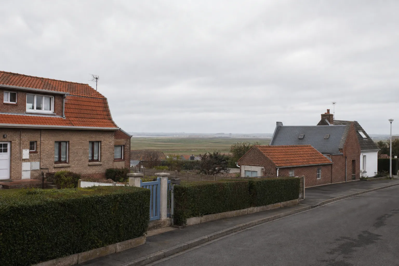Rue résidentielle de Marck dans le Pas-de-Calais, maisons de brique aux toitures en tuile, ciel couvert du littoral, photographie documentaire sans personne
